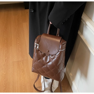 Detailed view of brown quilted leather backpack with embossed floral patterns and silver zipper