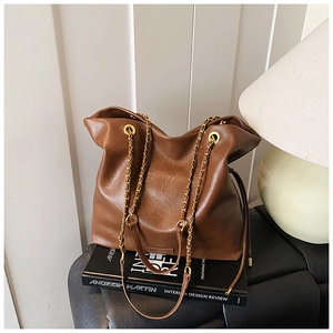 Detail of dark brown bucket bag with metal chain strap on minimalist background