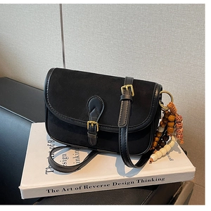Detail of a vintage black suede crossbody bag with ethnic beaded charm and gold buckle