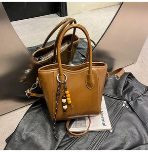 Détail du sac seau en cuir marron avec pendentif en bois et bandoulière réglable