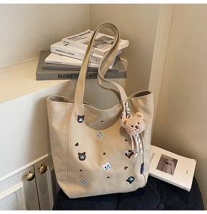 Close-up of beige canvas tote with cat embroidery, plush bear charm and wide straps