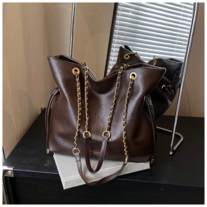Detail of dark brown leather bucket bag with gold chain strap and metal logo plaque
