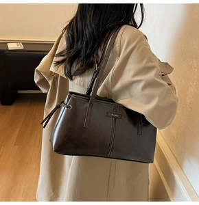 Detail of dark brown leather tote bag showing side drawstrings and fine metallic logo