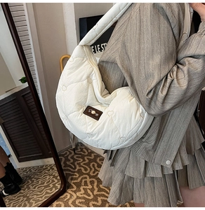 Close-up of white heart-quilted shoulder bag with brown leather patch and satin finish