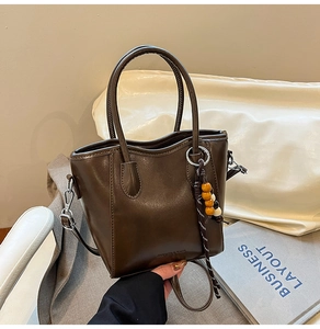 Détail de sac seau marron avec texte FASHION & BAGS et breloque en perles colorées