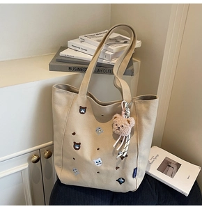 Detail of beige canvas tote with cat embroidery, plush bear charm, and brand label