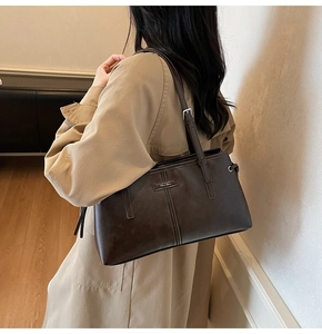 Detail of dark brown leather Boston bag with metal logo and fine stitching on shoulder strap
