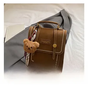 Brown vintage leather crossbody bag featuring white stitching and cute bear charm detail