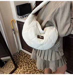 Detail of white heart-quilted hobo bag featuring a pearl-inlaid logo patch and soft texture