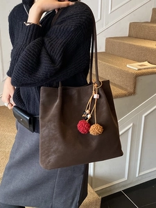Large dark brown suede tote bag with decorative plush charms shown in an indoor setting
