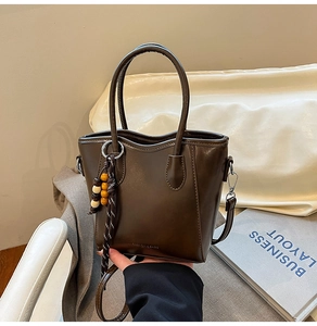 Détail du sac seau marron foncé avec pompon en perles de bois et logo de mode