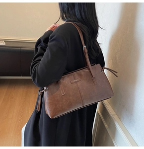 Detail view of brown vintage tote bag with drawstring tassels and adjustable strap on black coat