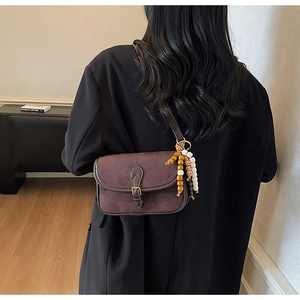 Detail of dark brown suede saddle bag featuring metal buckle and colorful beaded charm
