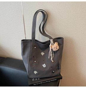 Close-up of dark grey canvas tote with colorful cat embroidery and plush bear charm