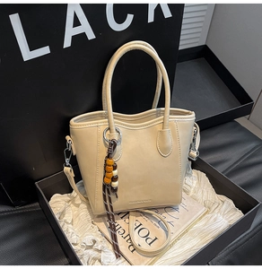 Détail du sac seau crème avec gland perlé dans un coffret cadeau élégant