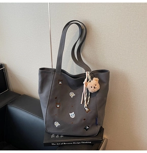 Detail of grey canvas tote bag featuring cute animal embroidery and plush bear pendant