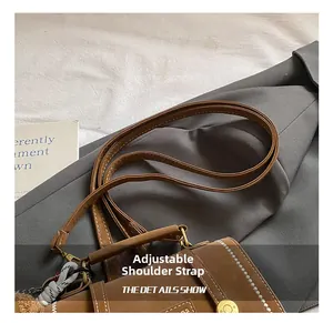 Detail of brown leather bag with white stitching and decorative plush pom-pom charm