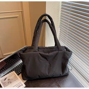 Close-up of a large black quilted nylon tote bag placed on a leather surface in a modern office