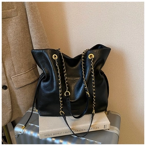 Detail of large black leather bucket bag with gold chain strap on luggage and coat