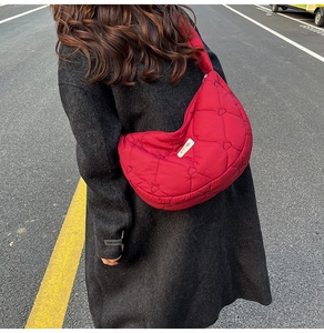 Close-up of red heart-quilted puffer crossbody bag worn with a charcoal wool coat