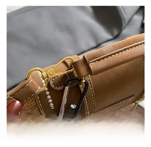 Detail view of gold lobster clasp and embroidery on brown leather travel backpack