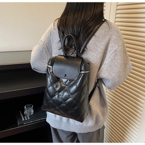 Detailed view of black quilted backpack featuring floral embossing and a top handle