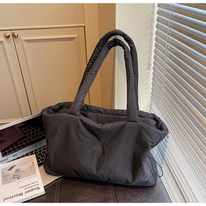Detail of a black quilted tote bag with padded handles next to a laptop and magazine