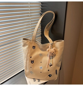 Detail of beige canvas tote with cat embroidery, plush bear charm, and side label tag