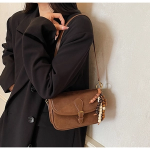Close-up of brown suede rectangular shoulder bag with vintage buckle and beaded charm detail