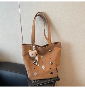 Detail of tan canvas tote bag featuring cute cat embroidery and plush bear charm