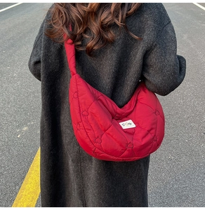 Outdoor street view of a red quilted puffy crossbody bag with heart-stitched patterns