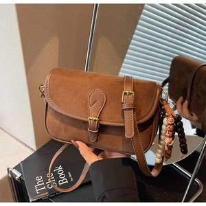 Close-up of brown suede crossbody bag featuring retro flap and colorful beaded charm