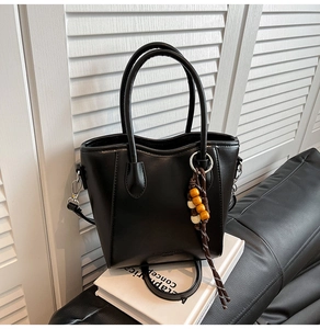 Détail du sac seau en similicuir noir avec pompon en perles de bois et bandoulière
