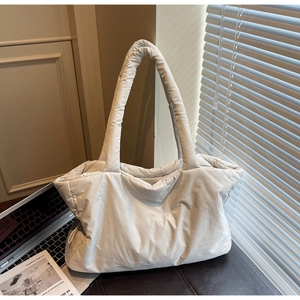 Detail of a beige quilted tote bag showing plush nylon texture and long shoulder strap