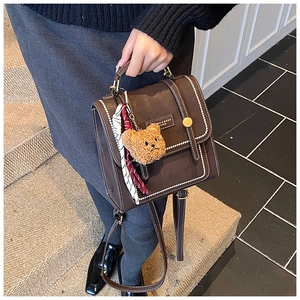 Detail of dark brown vintage mini backpack with contrast stitching and bear charm