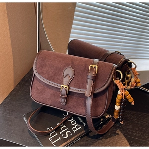 Detail of brown suede crossbody bag with vintage metal buckle and wooden bead charm