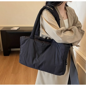 Detail of black quilted nylon tote bag featuring wide shoulder straps and side drawstring