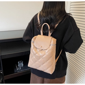 Quilted beige backpack with rhombic stitching shown on model in minimalist interior setting