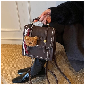 Detail view of coffee leather backpack with white stitching and bear charm accessory