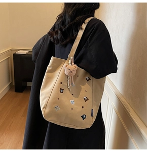Detail of embroidered cats on beige canvas tote bag with brown plush bear charm