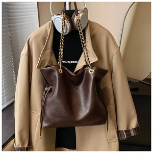 Detail of dark brown leather bucket bag with gold chain strap on beige trench coat