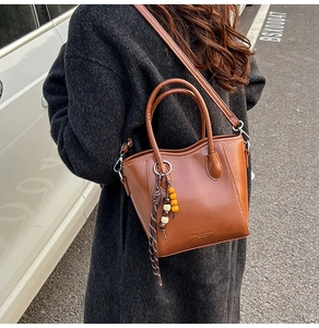 Détail d'un sac seau en cuir marron avec gland bohème et lettrage doré élégant