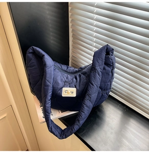 Detail of dark blue quilted crossbody bag with heart pattern stitching and pearl patch