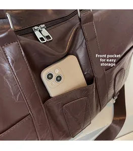 Gros plan du sac de voyage marron avec poche avant pour téléphone et texture en cuir grainé