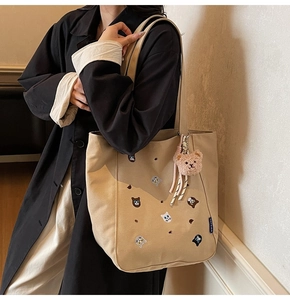 Detail of embroidered cat patterns and plush bear charm on beige canvas tote bag