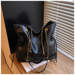 Detail of black leather bucket bag with gold chain strap and drawstring on wooden bench