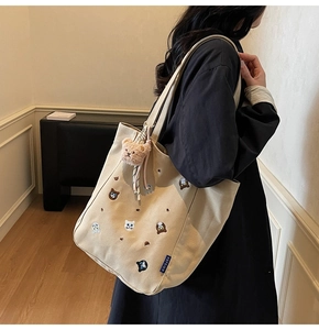 Detail of embroidered cat motifs and pink plush bear charm on beige canvas tote bag