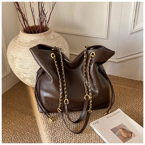 Detail of dark brown leather bucket bag with gold chain strap and drawstring closure