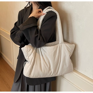 Close-up of a cream quilted nylon tote bag with wide shoulder strap worn by a model