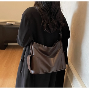 Detail view of large dark brown tote bag with side flap pockets on a matte leather finish